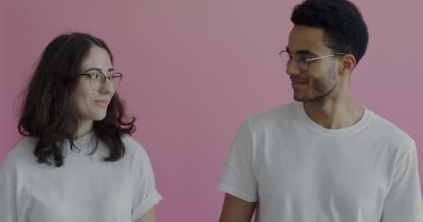 アフリカ系アメリカ人の男性と白人の女性が手を取り合ってピンクの背景で笑っています ロマンチックな関係を楽しんでいるカップル — ストック動画