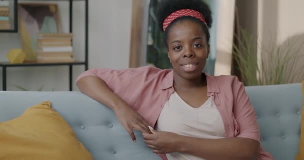 年轻快乐的女士坐在舒适的沙发上 微笑着看着相机 慢动作的肖像 青年和住宿概念 — 图库视频影像