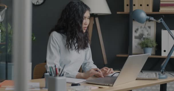 Амбициозная Азиатка Смотрит Экран Ноутбука Пишет Информацию Блокноте Столе Офисе — стоковое видео