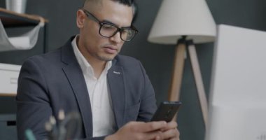 Akıllı telefonla mesajlaşan, ekranlara dokunan ve gülümseyen işadamının portresi ofiste iyi haberler alıyor. Elektronik ve iş insanları kavramı.