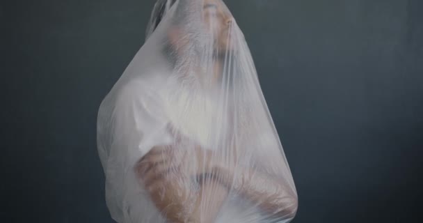 Porträtt Ung Afroamerikansk Man Kramar Sig Transparent Plastfilm Mot Grå — Stockvideo