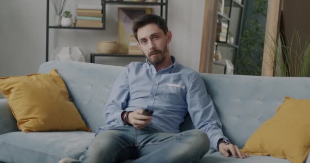 穿着时髦服装的年轻男子在家里用遥控装置在沙发上放松地看电视的画像 人与娱乐概念 — 图库视频影像