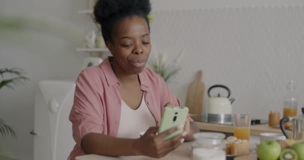 非洲裔美国女孩在家里吃含牛奶的麦片和使用智能手机的慢动作 营养和小玩艺儿概念 — 图库视频影像