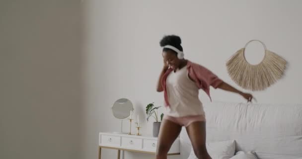 一个快乐的女孩头戴耳机 在公寓里跳着 在床上跳舞的慢动作肖像 现代生活方式和技术概念 — 图库视频影像
