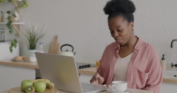 自宅のキッチンでオンラインビデオ通話のためのラップトップを使用して手を話し 手を振って楽しいアフリカ系アメリカ人女性 コミュニケーションとバーチャルミーティングのコンセプト — ストック動画