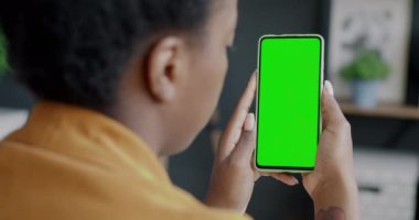 Ofiste elinde krom anahtar yeşil ekran akıllı telefon tutan kadın çalışanın omzunun üstünden. Modern aygıt ve mobil uygulama kavramı.