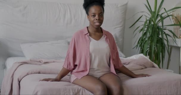 一个安静的非洲裔美国女人坐在床上 微笑着看着相机的慢镜头 国内内政和人的概念 — 图库视频影像