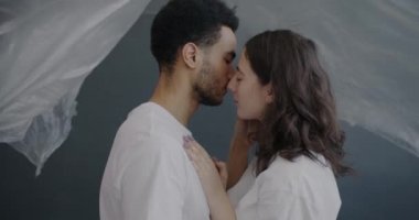 Çift ırklı çiftlerin yan yana durup birbirlerine bakmaları, üstlerine plastik film düşerken yüzlerine dokunmaları. İlişki ve aşk kavramı.