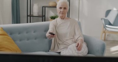 Mutlu yüzlü yaşlı güzel bir kadının portresi evde televizyon seyrediyor ve tek başına kanepede dinleniyor. Olumlu duygu ve eğlence kavramı.