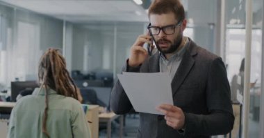 Kızgın işadamı cep telefonuyla konuşuyor. Yoğun ofiste duran belgeye bakıyor. Olumsuz duygu ve iş iletişimi kavramı.