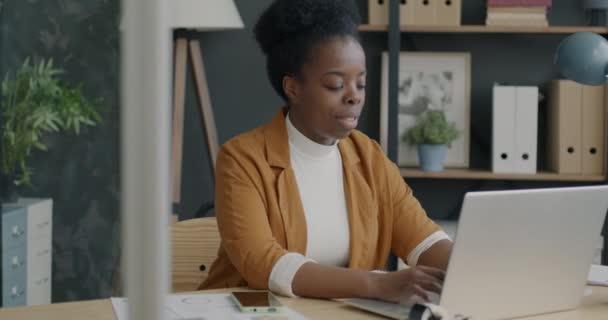 用笔记本电脑打字的非洲裔美国女商人的微笑集中在独自在办公桌前办公的工作上 创业和成功企业家的概念 — 图库视频影像