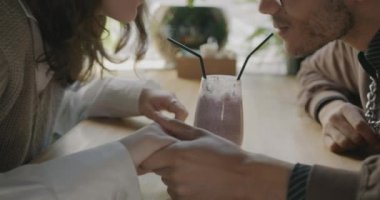 Kadın ve erkeğin el ele tutuşup bir bardaktan kokteyl içerken ve kafede tatlıyı yerken. İlişki ve yemek kavramı.