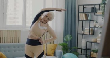 Yaşlı ve esnek bir kadının evde kollarını esneterek ve bükerek egzersiz yapması. Etkin yaşam tarzı ve emeklilik kavramı.