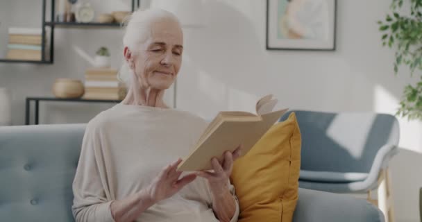 退休的女士在公寓的沙发上看书 享受着文学的放松 智能人和闲暇时间活动概念 — 图库视频影像