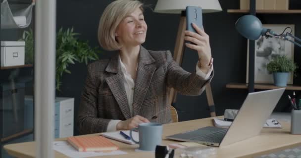 スマートフォンでオンラインビデオ通話を行い オフィス内で手を振って陽気な実業家の肖像画 技術と専門的なコミュニケーションの概念 — ストック動画