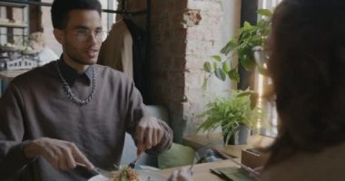 Afro-Amerikalı bir adamın portresi. Lezzetli yemekler yiyor ve kafede yemek yiyen bir kadınla konuşuyor. Beslenme ve ilişki kavramı.