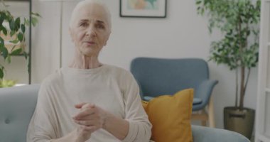 Evdeki online video görüşmesi sırasında mutlu bir gülümsemeyle konuşan ve el kol hareketi yapan emekli bir kadının portresi. Sanal toplantı ve uzaktan iletişim konsepti.