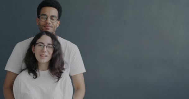 陽気なアフリカ系アメリカ人男性のスローモーションポートレート白人のガールフレンドを抱きかかえ 灰色の背景に笑みを浮かべて 肯定的な感情や人々の概念 — ストック動画