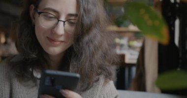 Akıllı telefon kullanan ve modern kafede kahve içen neşeli genç bayanın portresi. Eğlence ve modern teknoloji konsepti.