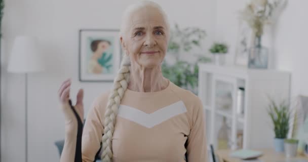 穿着时髦运动服站在家里挥手的老年妇女慢动作肖像 积极的老年人和公寓概念 — 图库视频影像