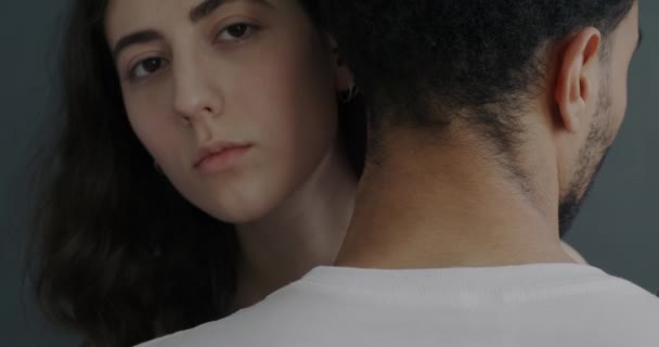 若い女性が男を抱きかかえ 灰色の背景にカメラを見てのクローズアップ肖像画 人間の感情の概念 — ストック動画