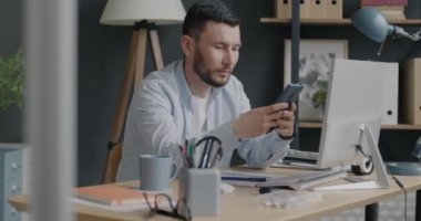 Genç girişimci akıllı telefon taraması yapıyor sonra da ofiste çalışırken not defterine bilgi yazıyor. İletişim ve çalışanlar konsepti.