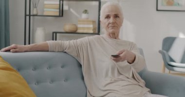Mutlu emekli kadın portresi TV izlerken gülüyor ve kameraya bakıyor evdeki kanepede dinleniyor. Eğlence ve televizyon konsepti.