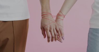 Kırmızı iple sarılmış erkek ve kadın elleri pembe arka plana dokunuyor. Romantik bağ ve sevgi dolu ilişki kavramı.