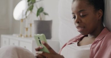 Akıllı telefon kullanan, içeriğin tadını çıkaran ve evde oturup gülen neşeli genç bir kadın. Elektronik ve modern teknoloji konsepti.