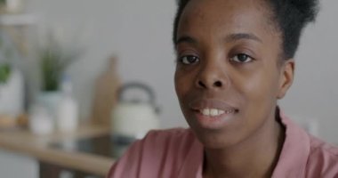 Rahatlamış Afro-Amerikan kadın portresi. Mutfaktaki neşeli yüzüyle kameraya gülümsüyor. Gençlik ve gündelik hayat kavramı.