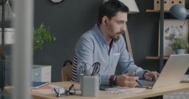 Yaratıcı bir çalışan dizüstü bilgisayarla yazı yazıyor ve ofiste kulaklıkla müzik dinlemekten zevk alıyor. Modern teknoloji ve eğlence konsepti.