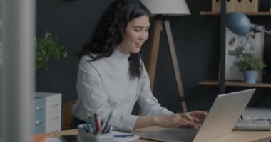 Tasasız genç bayan laptopla çalışıyor ve dans ediyor. Ofiste müzik dinliyor, eğleniyor. Modern teknoloji ve eğlence iş kavramında.