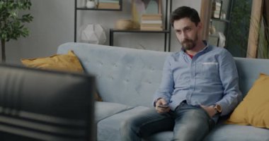 Tasasız genç adam portresi televizyon seyrediyor. Evde boş vakitlerde kanepede oturuyor. Eğlence ve kitle iletişim araçları kavramı.