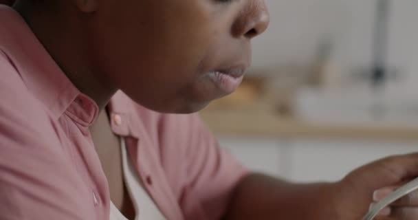 空腹のアフリカ系アメリカ人の少女のクローズアップは アパートのキッチンで朝食のための牛乳とシリアルを食べる 食品と健康的な栄養の概念 — ストック動画