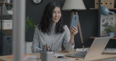 Kaygısız Asyalı kadın konuşuyor, el sallıyor ve iş yerindeki online video görüşmesi sırasında eğleniyor. İş kadını partnerle iletişimden keyif alıyor.