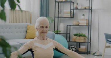 Yaşlı sporcunun portresi halterleri kaldırıyor yoga minderinde oturuyor evde spor yapıyor. Moda kıyafetli emekli kadın yalnız çalışıyor..