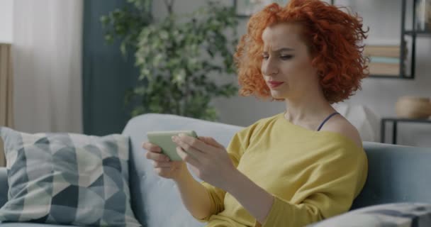 自宅で余暇活動を楽しんでいるスマートフォンで遊んでいる女性ゲーマーの肖像 近代的なデバイスとエンターテイメントのコンセプト — ストック動画