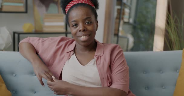 Retrato Encantadora Dama Afroamericana Sonriendo Sentada Sofá Apartamento Mirando Cámara — Vídeos de Stock