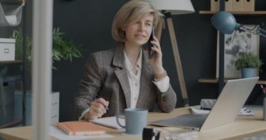 Cep telefonuyla konuşan ve ofis odasında dizüstü bilgisayarla çalışan girişimci portresi. Modern teknoloji ve kariyer geliştirme kavramı.