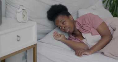 Pijamalı, uykulu Afro-Amerikan kadın portresi. Evdeki yatakta çalar saati kapatarak uyanıyor. Sabah ve insan konsepti.