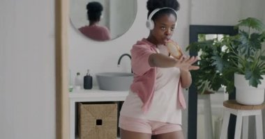 Pijamalı güzel Afrikalı Amerikalı kızın portresi banyodaki kulaklıklarda müzik eşliğinde şarkı söyleyip dans ediyor. Gençlik ve eğlence zamanı konsepti.