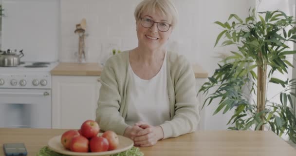 Retrato Cámara Lenta Alegre Mujer Mayor Sentada Cocina Mesa Sonriendo — Vídeos de Stock
