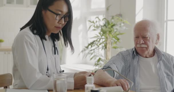 Азиатка Врач Белом Халате Проверяет Кровяное Давление Осматривает Пациента Старшего — стоковое видео