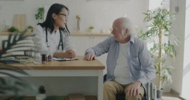 Bakıcı doktor hastalara dokunuyor. Daireyi ziyaret ederken tekerlekli sandalyedeki yaşlı adama destek oluyor. Emeklilik ve tıbbi bakım kavramı.