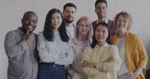 カメラを見て笑顔でオフィスに立っている多様なグループの同僚の陽気な若い人たち キャリアと職場を楽しむ役員のチーム — ストック動画