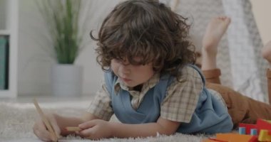 Sevimli küçük çocuk resim çiziyor evde yerde yatıyor ve sanatla meşgul. Çocuk gelişimi ve yaratıcı sanatlar konsepti.