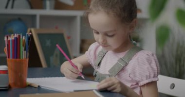 Evde boş zamanlarında yaratıcı aktivitelerin tadını çıkaran kalemlerle çizen sevimli küçük bir kız. Mutlu çocukluk ve sanatsal meslek kavramı.
