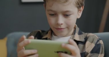 Akıllı telefonlu online video oyunu oynayan neşeli çocuk dairede kaygısız hareketlerin keyfini çıkarıyor. Oyun aleti ve mutlu çocukluk konsepti.
