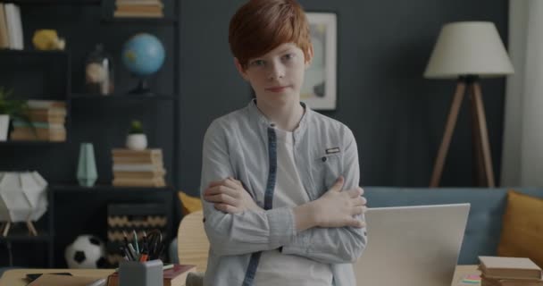 自宅に立ってカメラを見ている10代の少年のスローモーションポートレート 背景に見える家具のコンピュータテーブル付きのモダンな部屋のインテリア — ストック動画