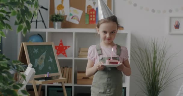自宅でお誕生日を祝うキャンドル付きパーティー帽子保持ケーキを身に着けている幸せな子供のスローモーションポートレート 休日と子供時代のコンセプト — ストック動画